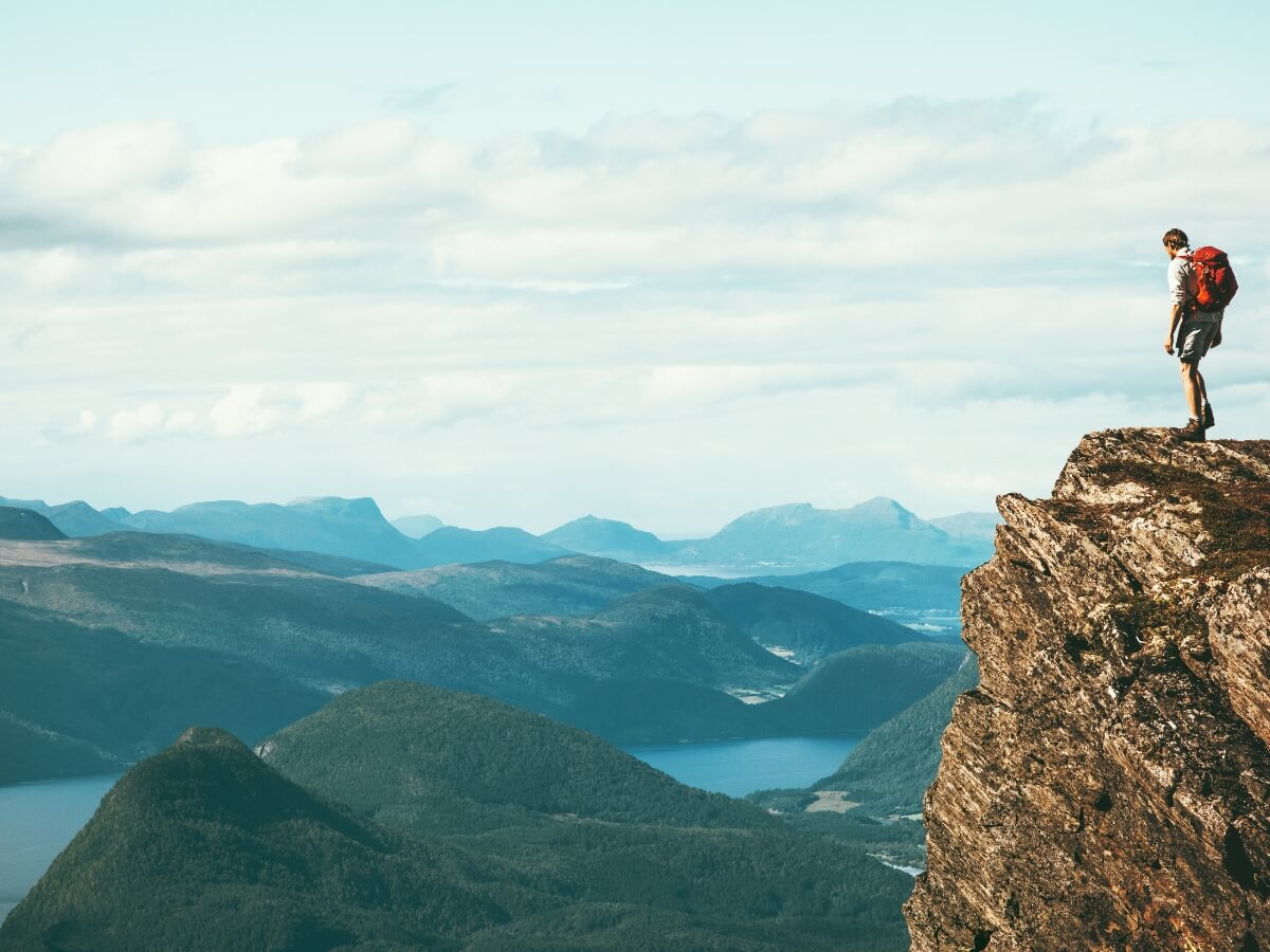Turista na vrchole skaly s výhľadom na prírodu.