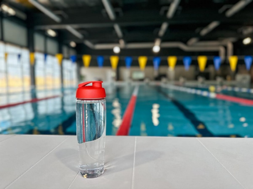 Sklenená fľaša naplnená vodou položená pri plaveckom bazéne.