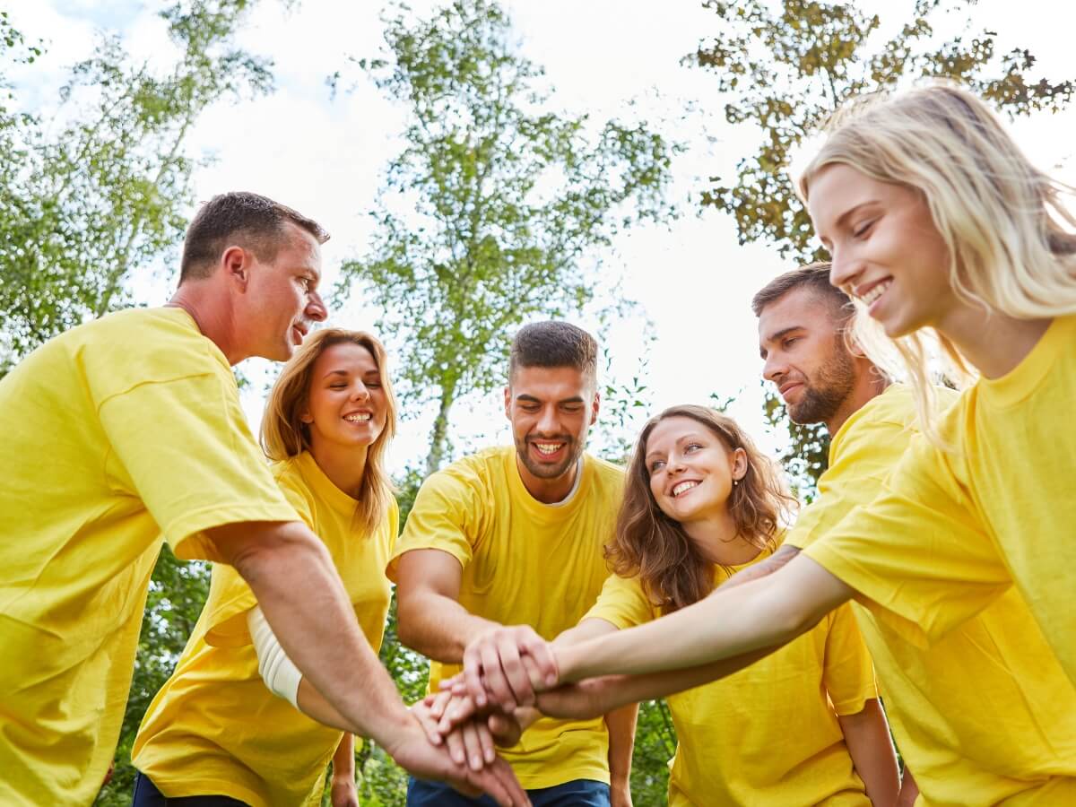 Tím ľudí v žltých tričkách so spojenými rukami počas športového teambuildingu.