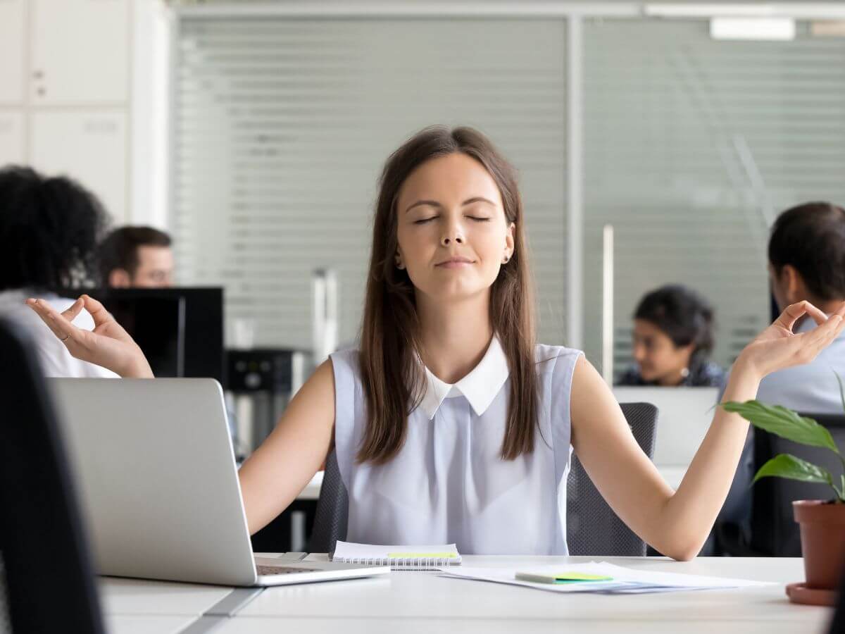 Žena v meditačnej pozícii medzi kolegami na pracovisku.