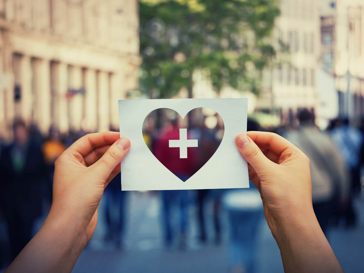 Človek držiaci v mestskom prostredí vystrihnuté srdiečko z papiera.