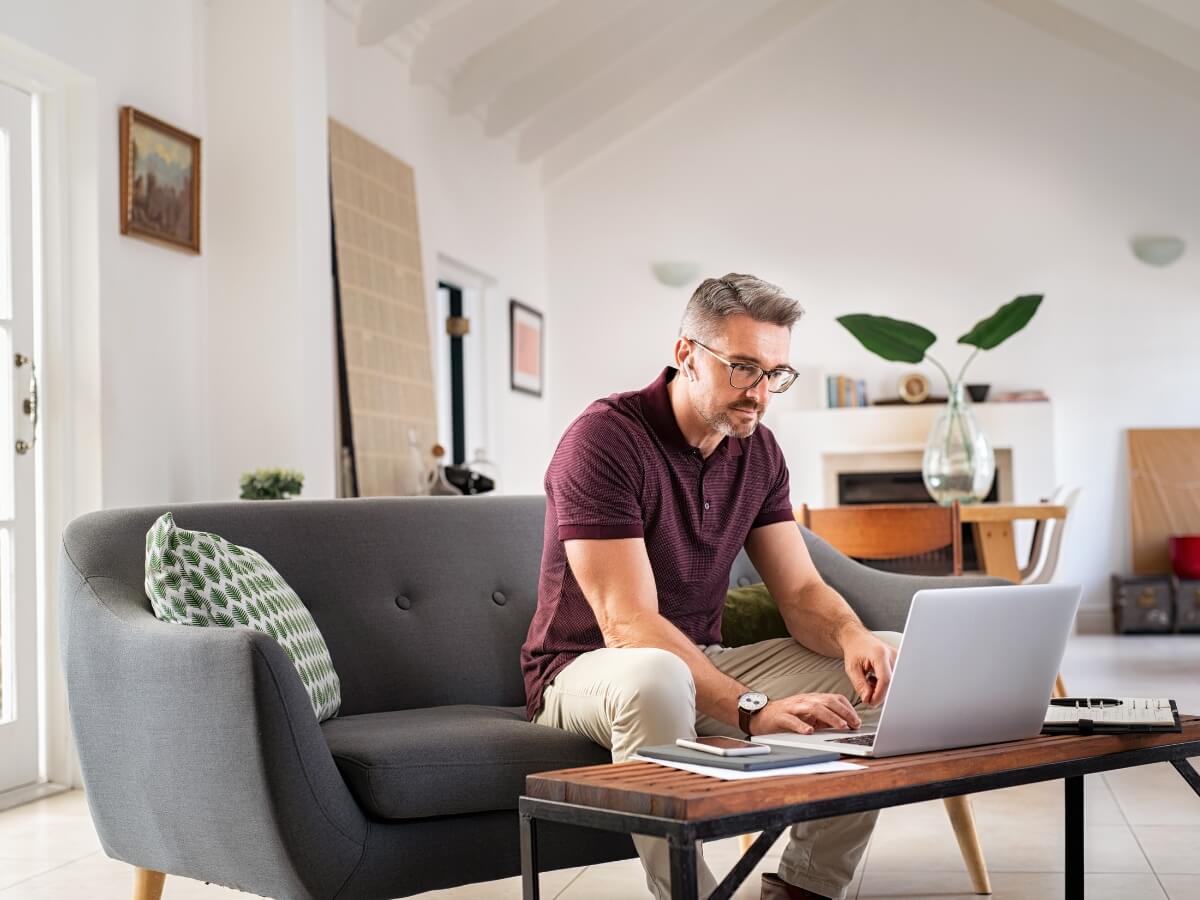 Muž pracujúci z domu za počítačom sediaci na gauči.