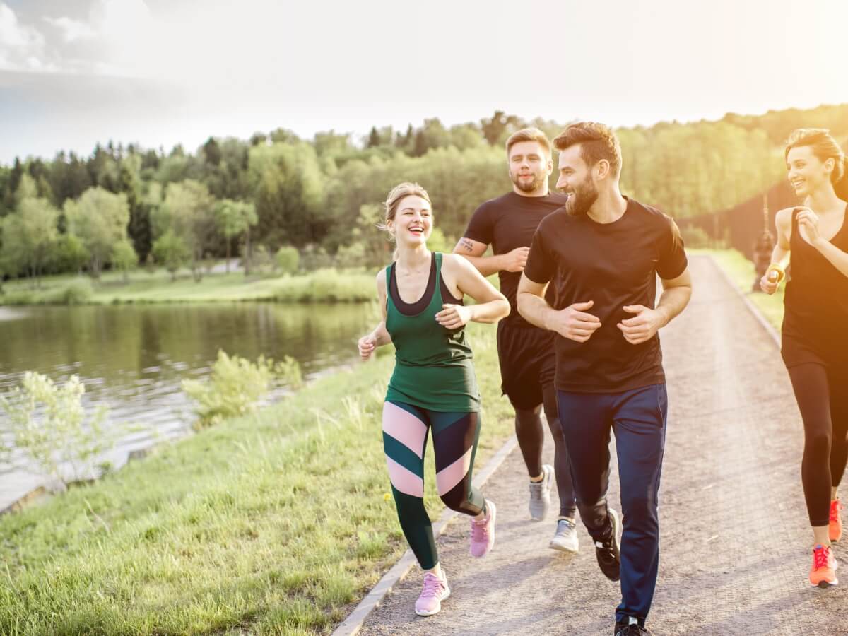 Skupina priateľov behá spolu v prírode pri jazere.